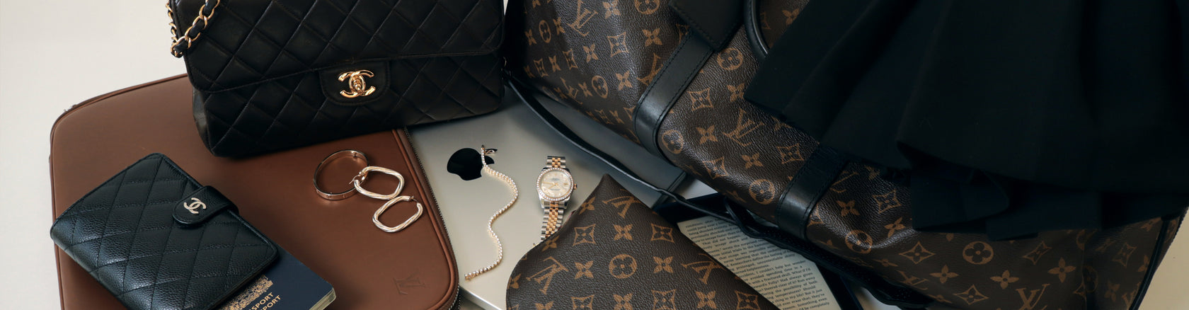 Winter travel essentials flat lay from Modaselle: pre-owned Louis Vuitton monogram travel bag and pouch, Chanel black classic flap bag and wallet, gold watch and jewelry